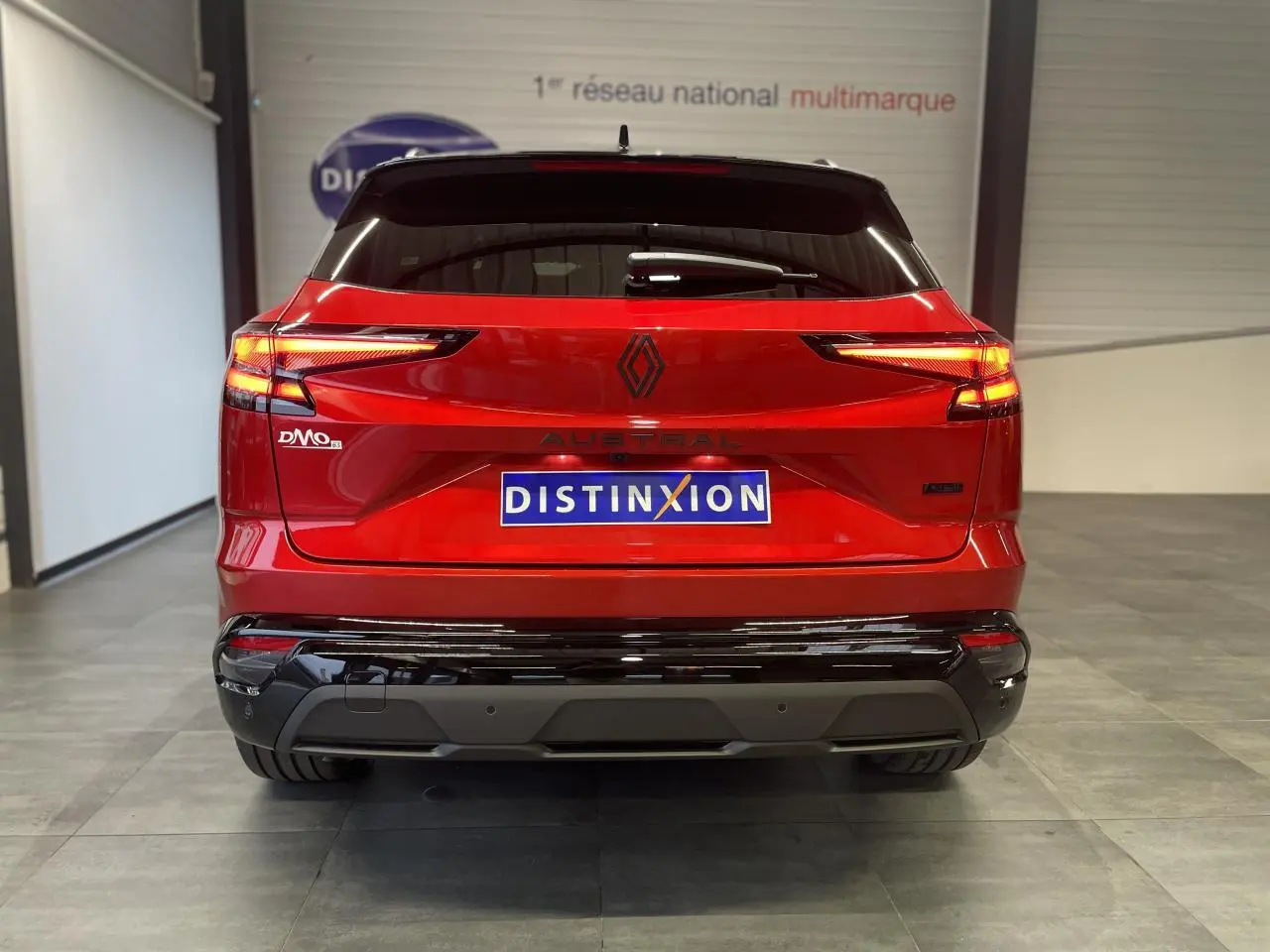 Vue arrière d'un Renault Austral rouge métallisé avec toit noir et logos noirs brillants dans un showroom.