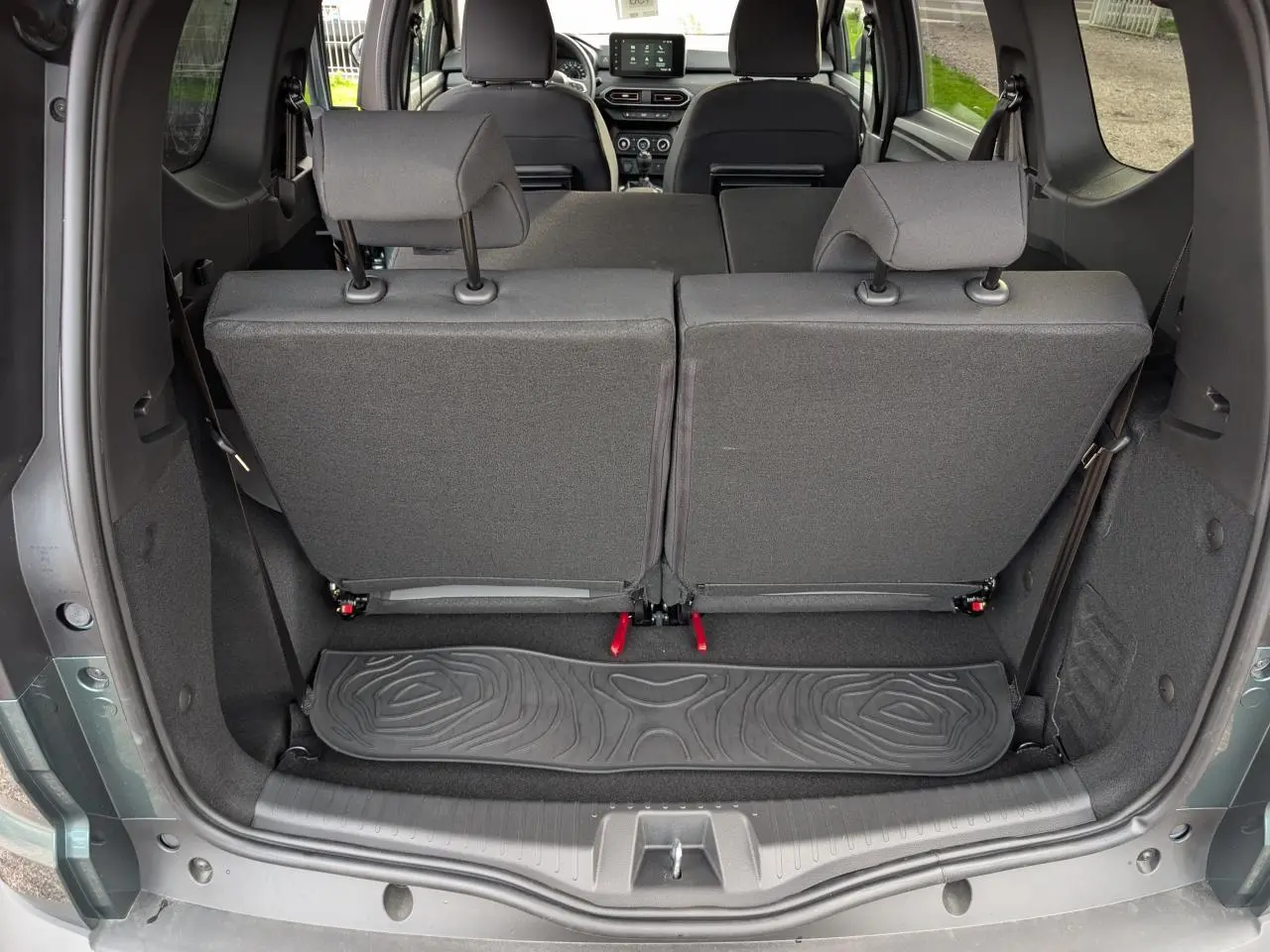 Vue arrière du coffre ouvert du Dacia Jogger gris métallisé 2025, montrant les sièges arrière rabattables et tapis de sol caoutchouc.