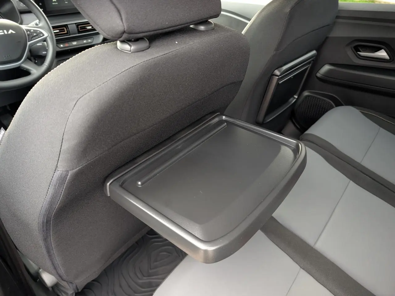 Vue intérieure arrière droite du Dacia Jogger 2025 avec tablette rabattable sur siège avant et sellerie gris clair et noir.