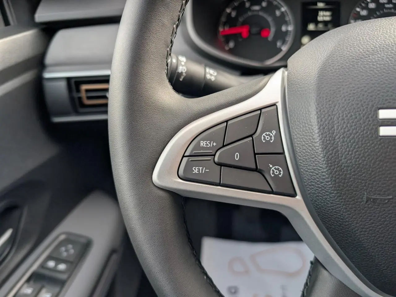 Gros plan sur les commandes du régulateur de vitesse au volant noir du Dacia Jogger 2025, intérieur gris acier.