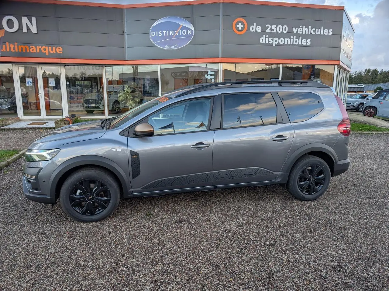 Vue de profil côté gauche d'un Dacia Jogger gris métallisé avec jantes noires et rétroviseurs brun cuivré.