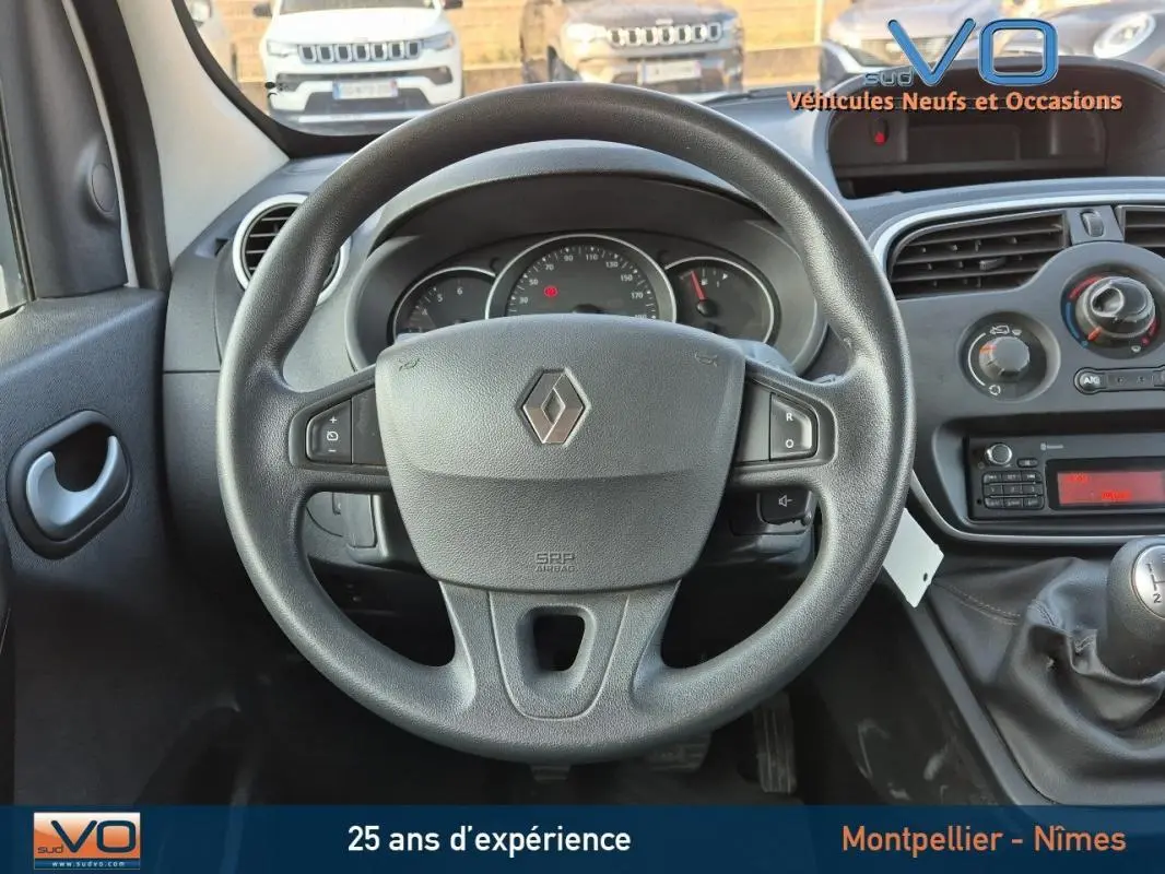 Vue intérieure centrée sur le volant Renault du Kangoo blanc 2016 avec tableau de bord et levier de vitesse manuel visibles.