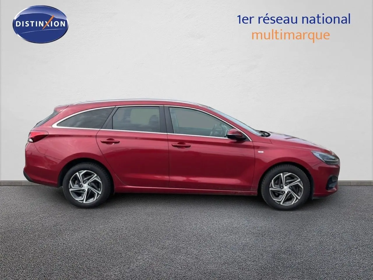 Profil latéral droit d'une Hyundai i30 SW 2023 rouge Sunset Red Metal avec jantes alliage bicolores.