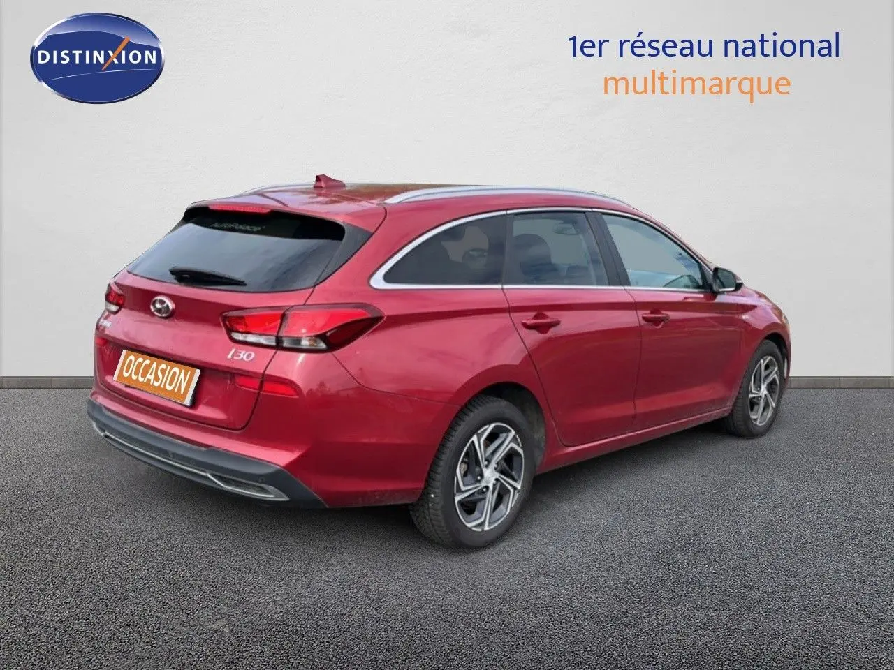 Vue 3/4 arrière droite d'une Hyundai i30 SW 2023 rouge Sunset Red Metal avec jantes alliage bicolores et vitres teintées.