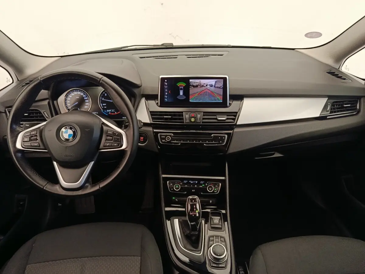 Vue intérieure avant de la BMW Série 2 Gran Tourer 218i Lounge 2022, tableau de bord noir avec écran central et volant cuir alu.