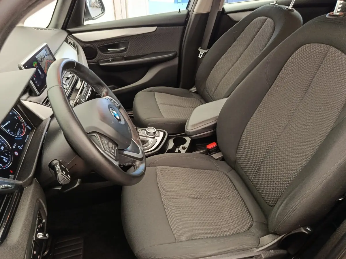 Vue intérieure côté conducteur de la BMW Série 2 Gran Tourer 218i Lounge 2022, sièges tissu gris et volant cuir multifonctions.