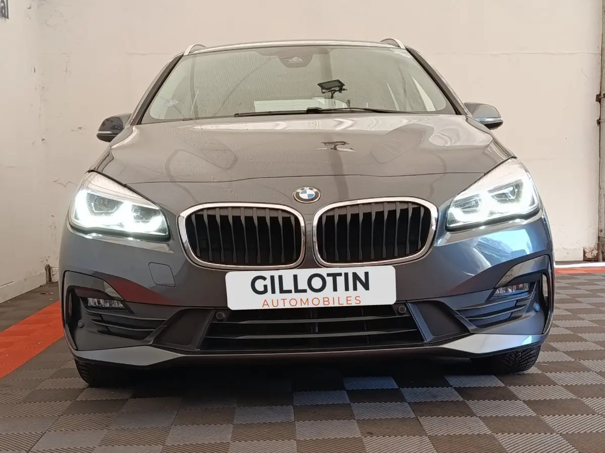 Vue frontale d'une BMW Série 2 Gran Tourer 218i Lounge gris clair avec phares LED allumés et calandre double haricot.