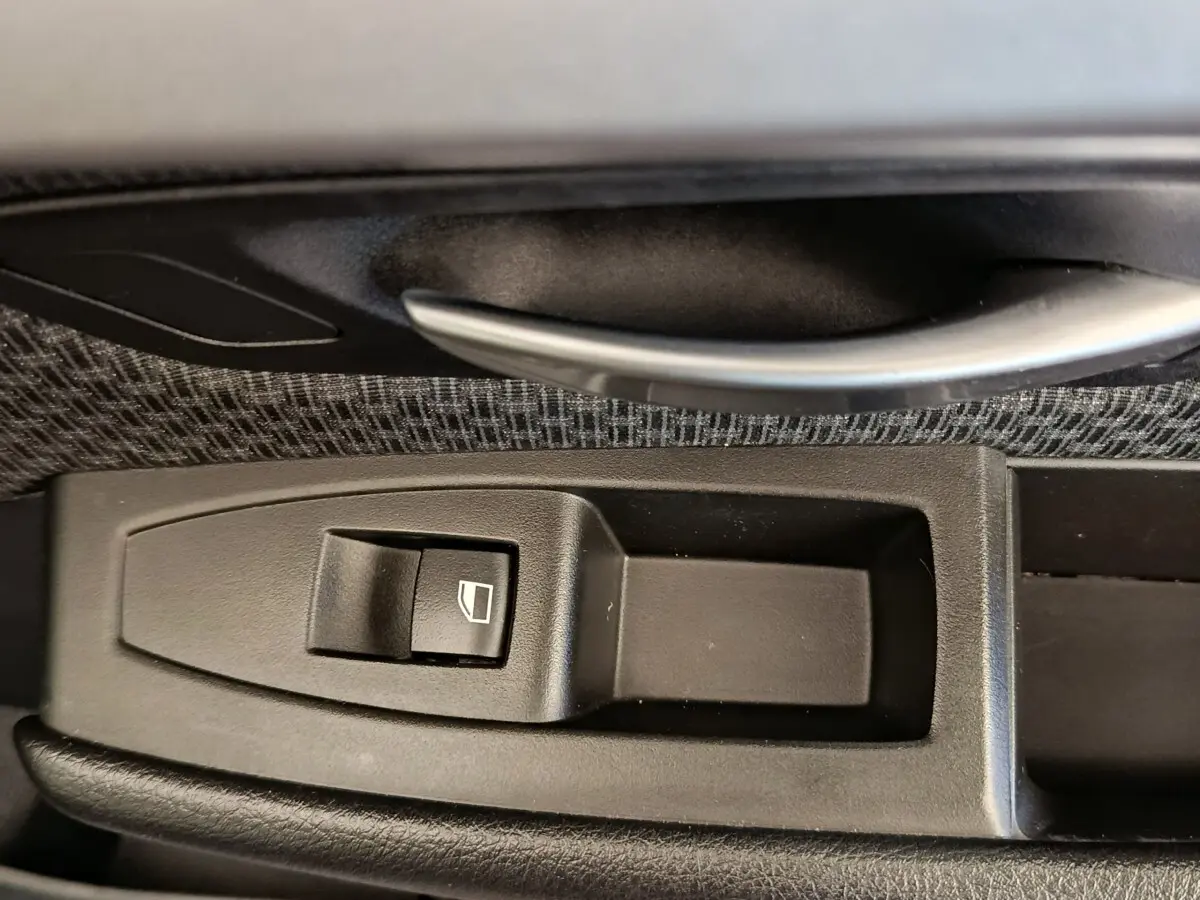 Gros plan sur la commande de lève-vitre côté conducteur avec poignée alu, intérieur tissu gris de la BMW Série 2 Gran Tourer 218i Lounge.