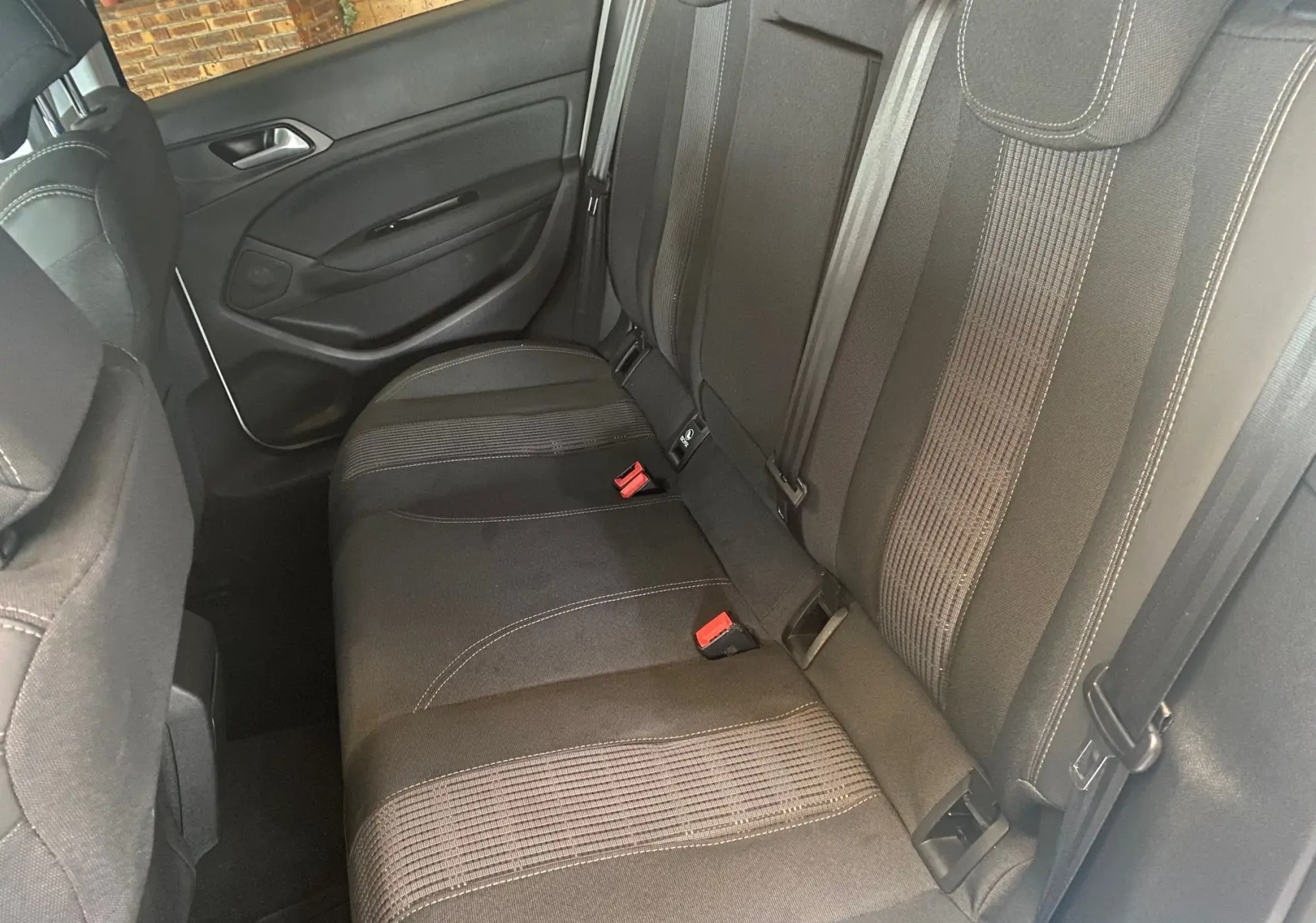 Vue intérieure sur les sièges arrière noirs en tissu de la Peugeot 308 Allure blanche de 2020, avec ceintures et appuie-têtes visibles.