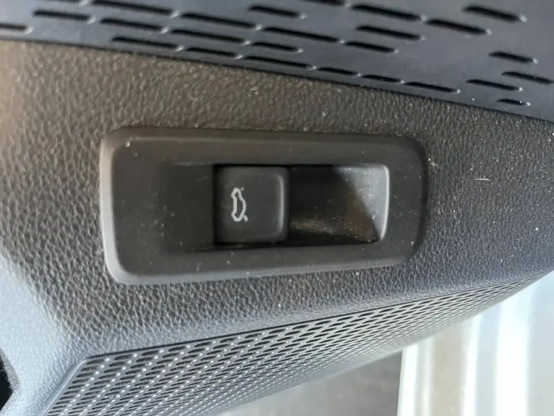 Gros plan sur le bouton d'ouverture du coffre dans l'habitacle noir d'une Skoda Octavia Combi blanche.