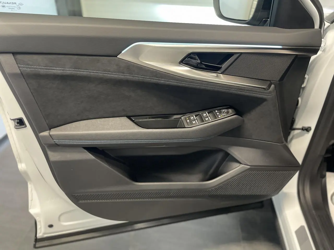 Gros plan sur la porte avant gauche du Renault Austral blanc nacré satin, avec garniture Alcantara et commandes électriques.