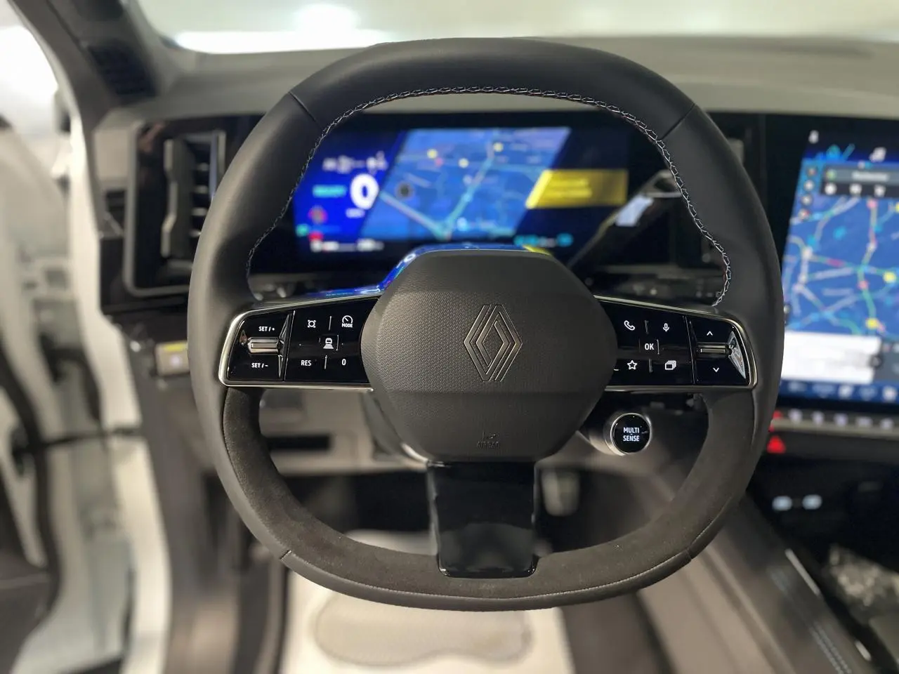 Volant Alcantara avec surpiqûres tricolores et logo Renault, tableau de bord numérique du Renault Austral 2025 visible en arrière-plan.