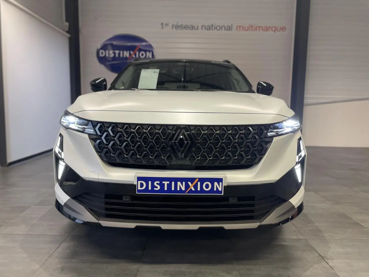 Vue frontale d'un Renault Austral blanc nacré satin avec calandre noire et feux LED allumés en showroom.