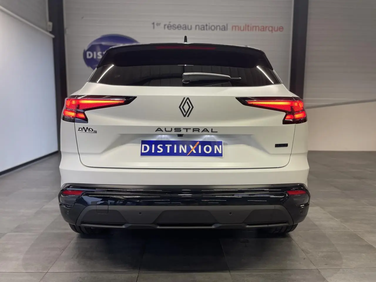 Vue arrière d'un Renault Austral blanc nacré avec toit noir et feux LED allumés en intérieur showroom