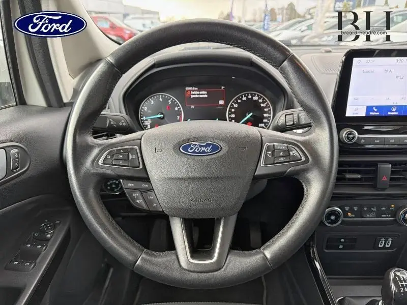 Vue intérieure centrée sur le volant cuir noir du Ford EcoSport blanc avec tableau de bord et écran tactile visible.