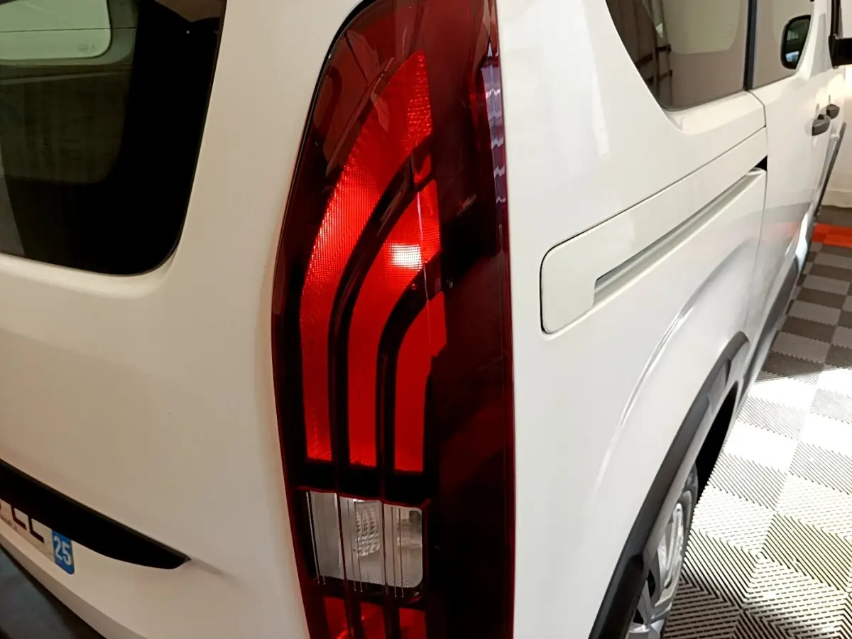 Gros plan sur le feu arrière droit rouge du Peugeot Rifter blanc, avec partie latérale et roue visible en intérieur.