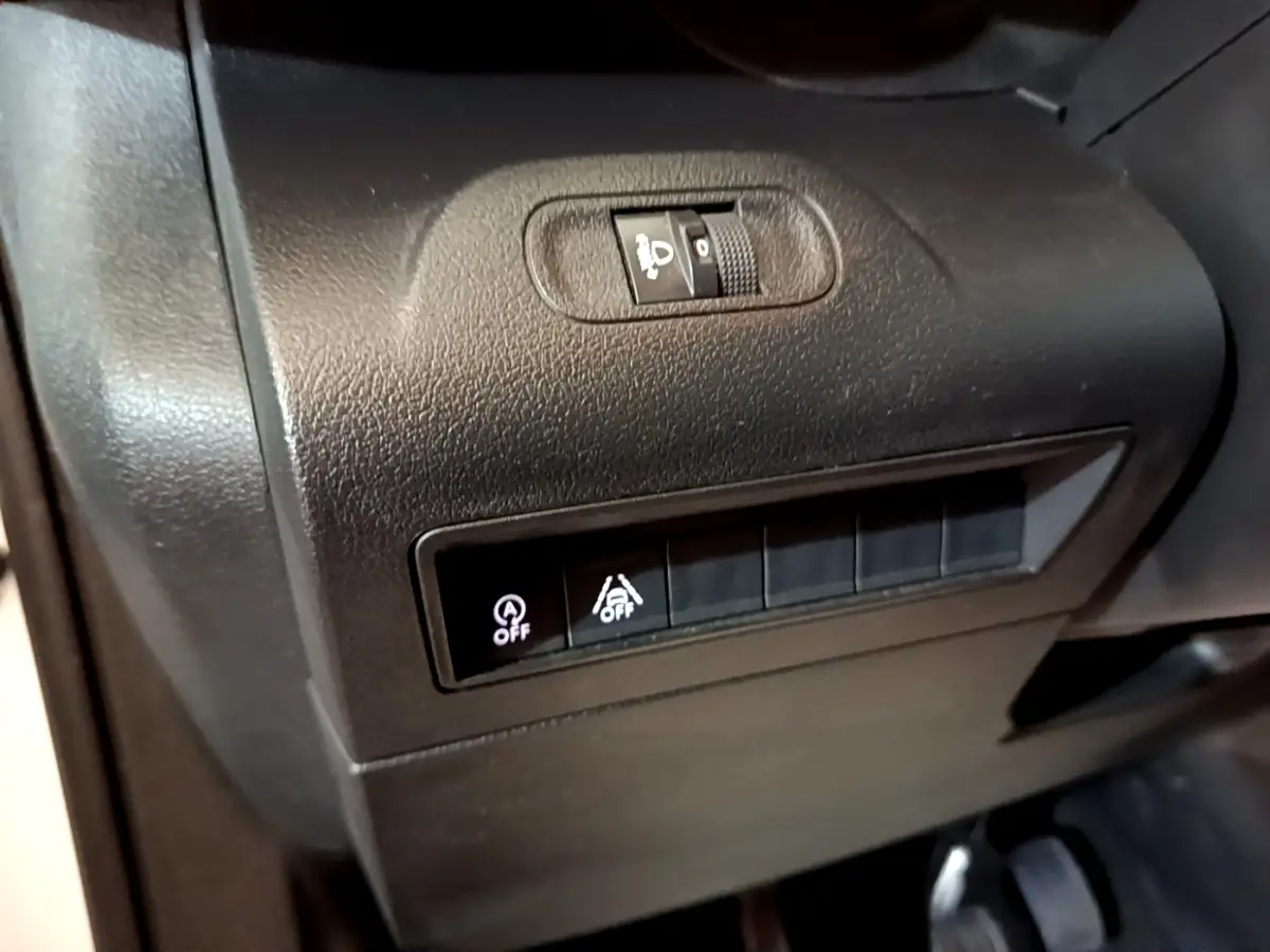 Gros plan sur les commandes de réglage des phares et désactivation de l'assistance au freinage du Peugeot Rifter blanc 2019.