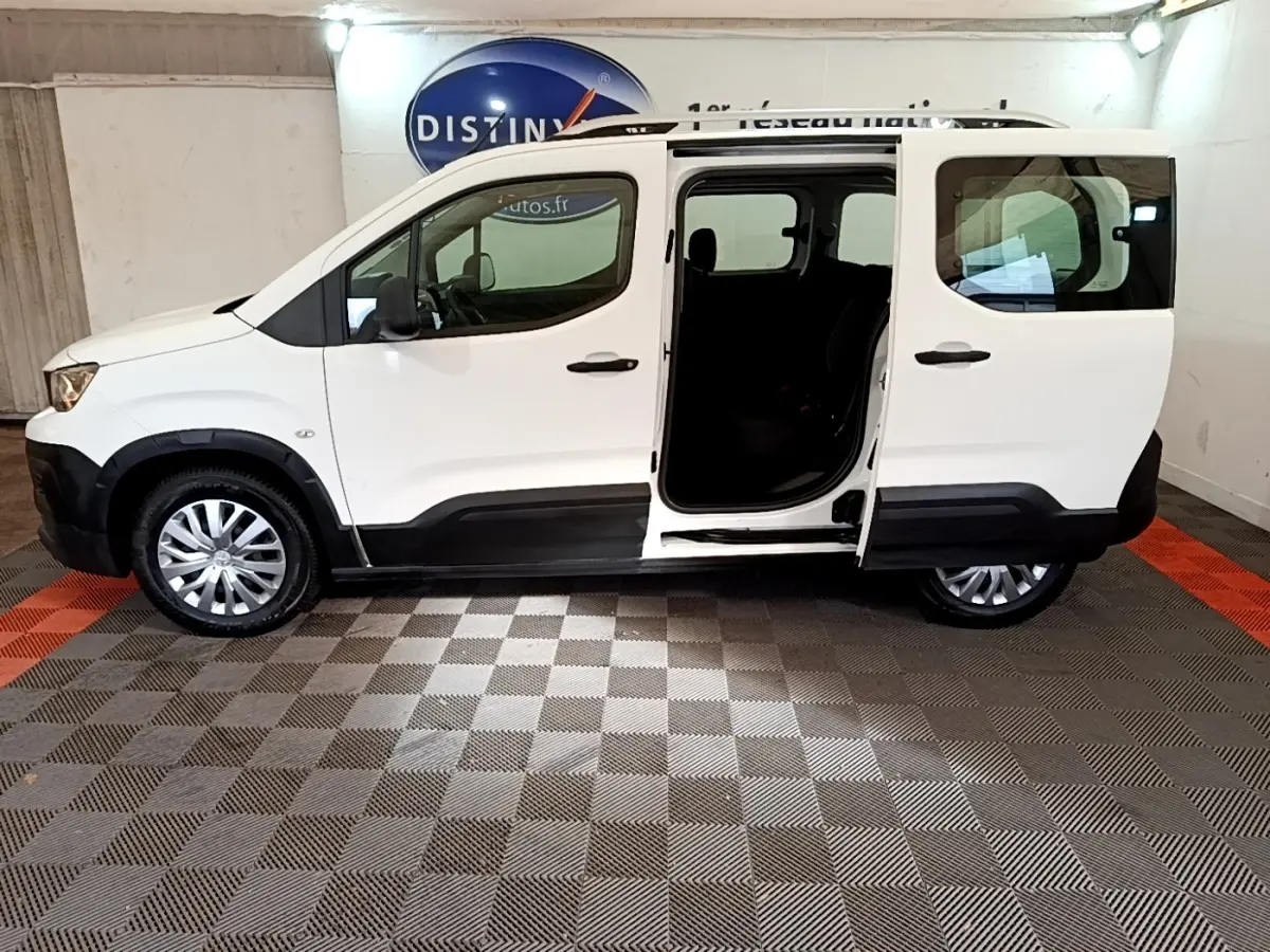 Vue latérale droite d'un Peugeot Rifter blanc 2019 avec porte coulissante arrière ouverte en intérieur showroom.