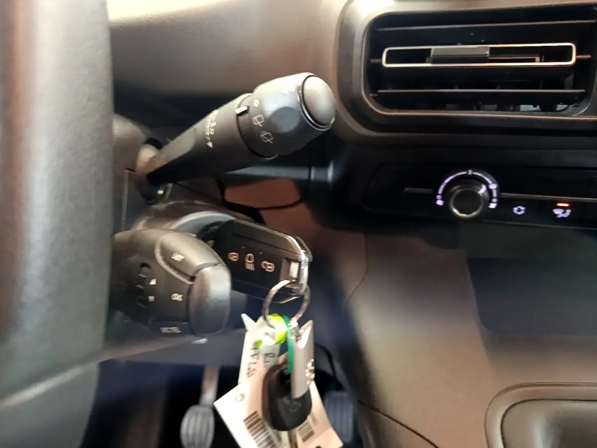 Gros plan intérieur sur la colonne de direction et clé de contact du Peugeot Rifter blanc, avec commande d’essuie-glace et ventilation.
