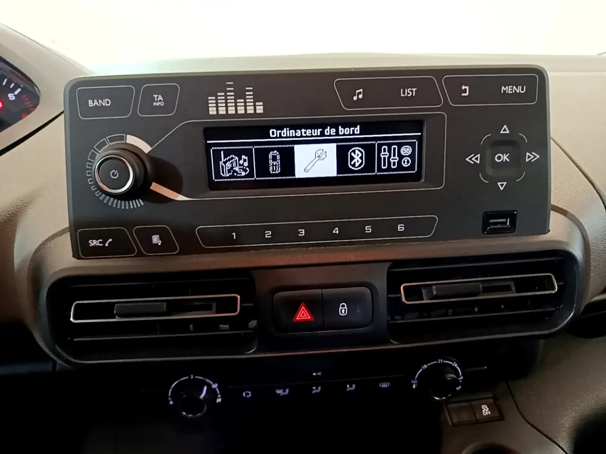 Vue rapprochée du tableau de bord noir du Peugeot Rifter blanc 2019, affichage multi-fonctions et commandes centrales visibles.