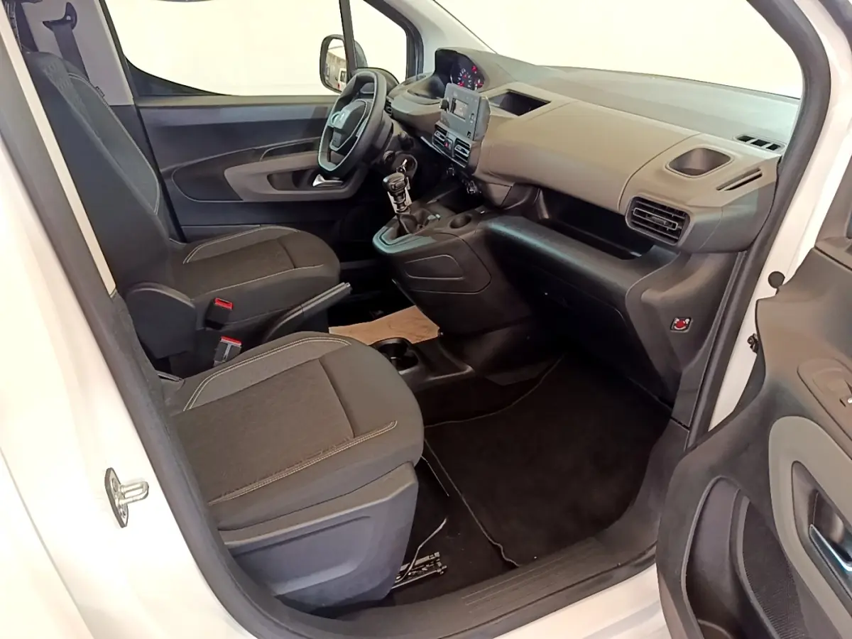 Vue intérieure côté conducteur du Peugeot Rifter blanc 2019, montrant tableau de bord, volant et sièges tissu noirs.