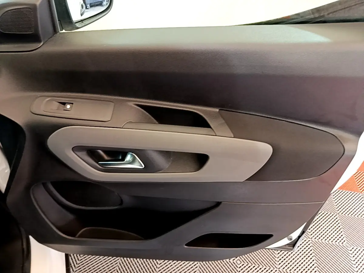 Vue rapprochée de la porte avant gauche intérieure du Peugeot Rifter blanc, avec poignée argentée et panneau noir/gris.