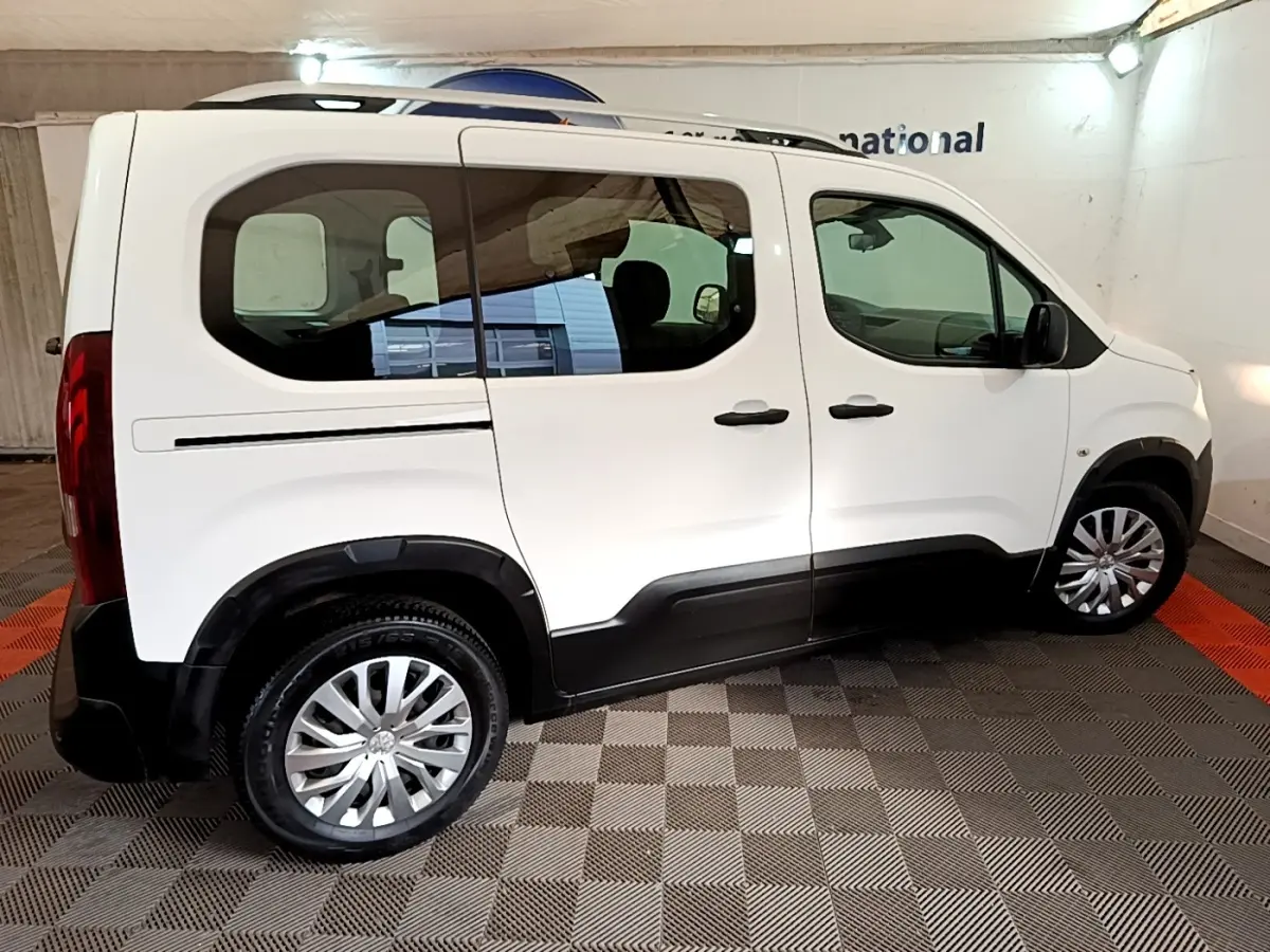 Vue de profil côté droit d'un Peugeot Rifter blanc 2019 avec barres de toit et protections noires sur les bas de caisse.