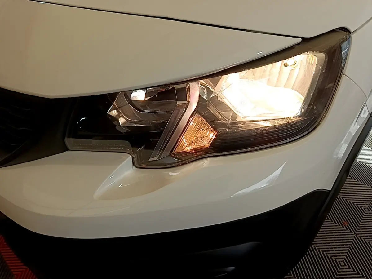 Gros plan sur le phare avant droit allumé d’un Peugeot Rifter blanc, mettant en valeur les détails du bloc optique.