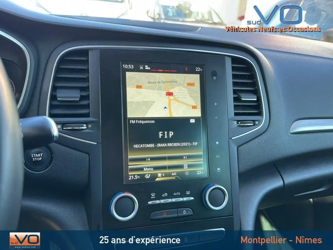 Vue rapprochée du tableau de bord de la Renault Mégane IV beige, avec écran tactile affichant la navigation et la radio FIP.