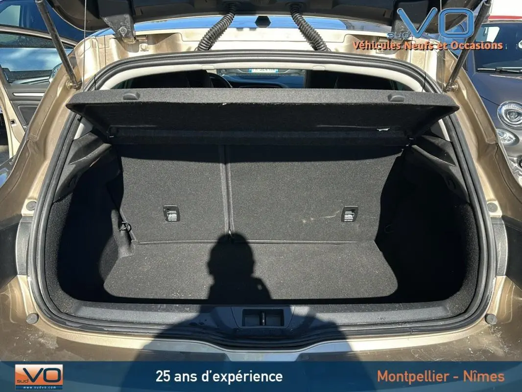 Coffre ouvert vu de l'arrière d'une Renault Mégane IV beige, montrant l'espace de chargement vide et propre.