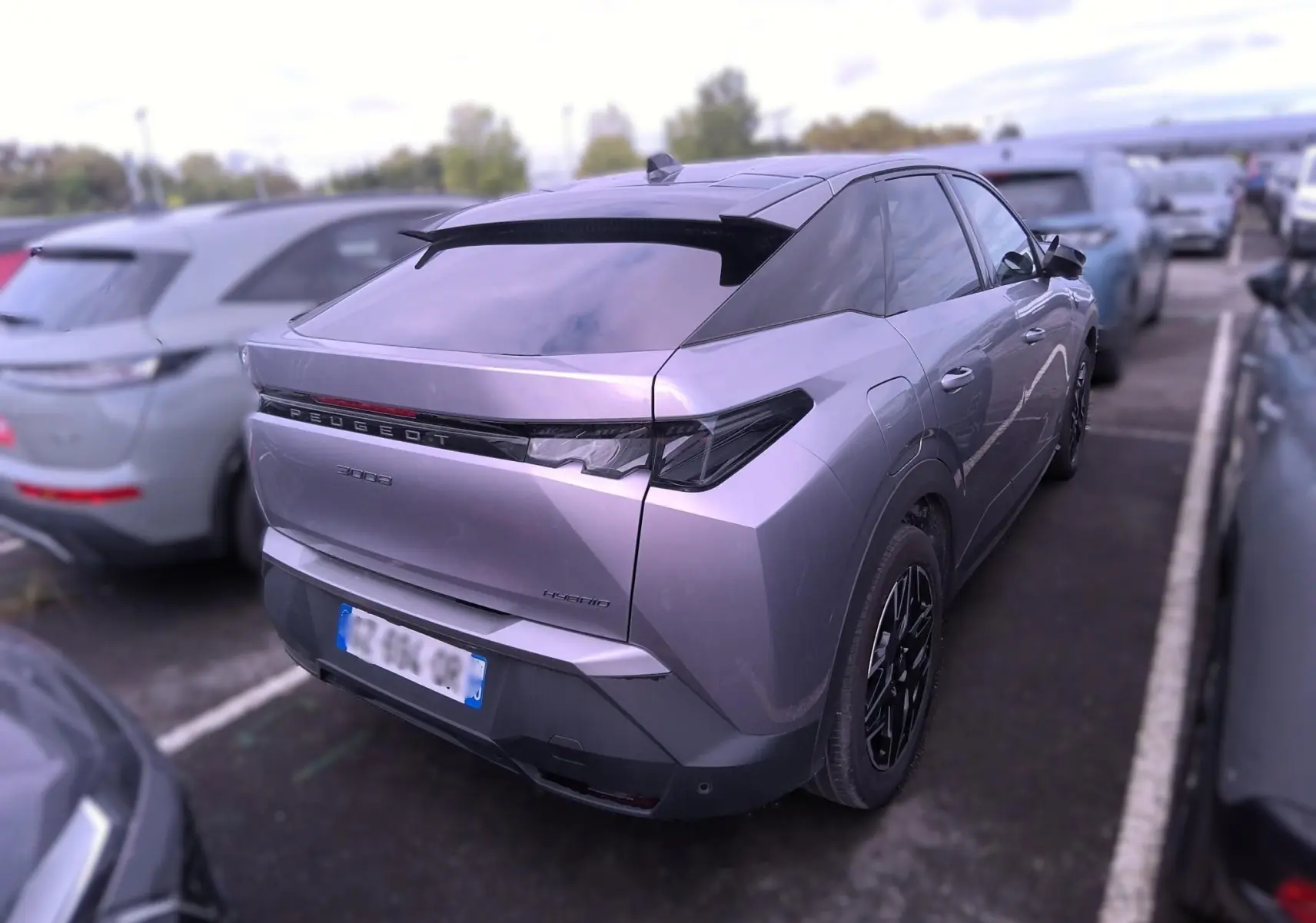 Vue 3/4 arrière droite d’un Peugeot 3008 gris 2024 hybride avec feux arrière étirés et jantes noires.