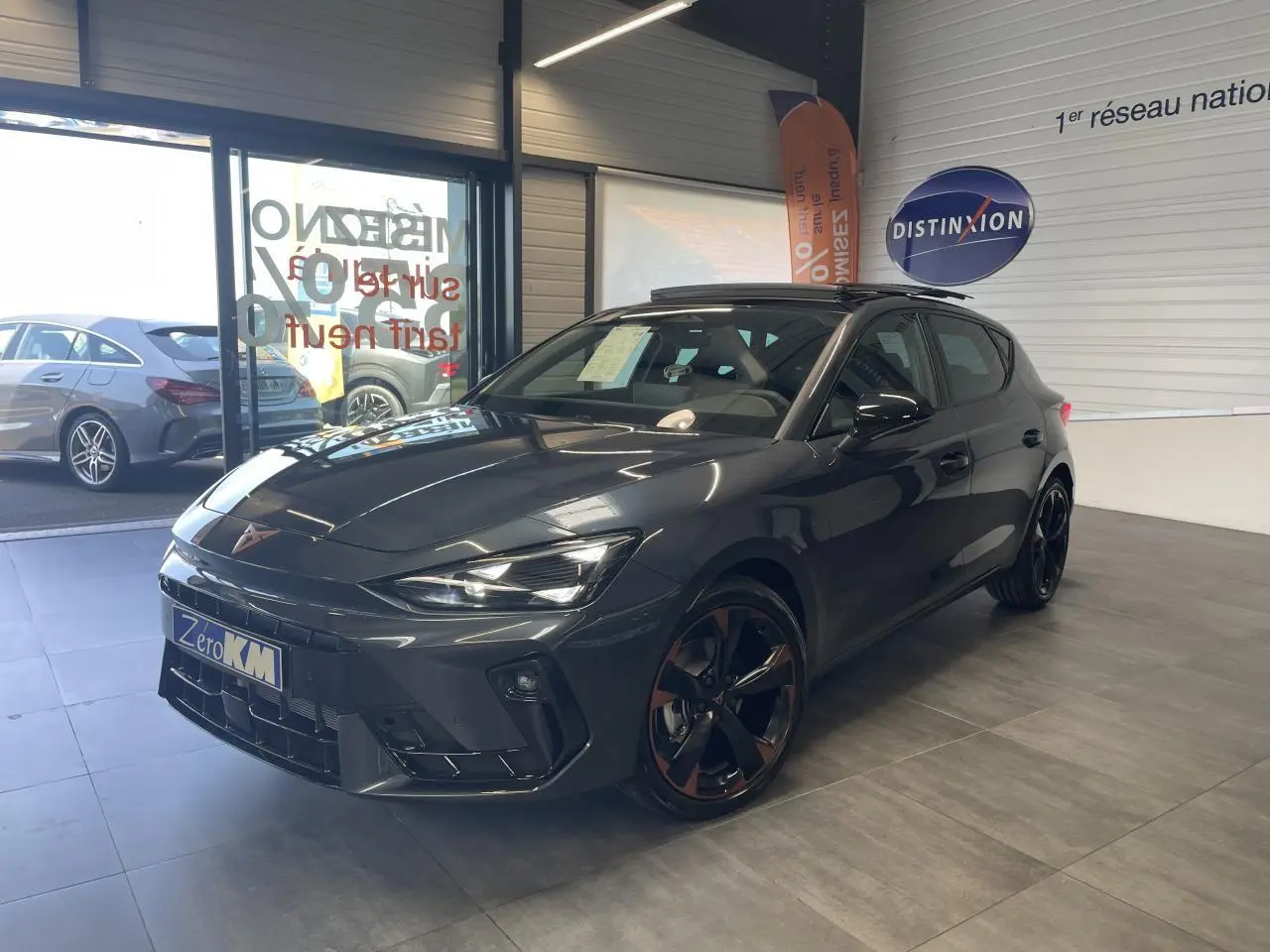 Vue 3/4 avant d'une CUPRA Leon gris magnetic avec jantes cuivrées et toit ouvrant panoramique en showroom.