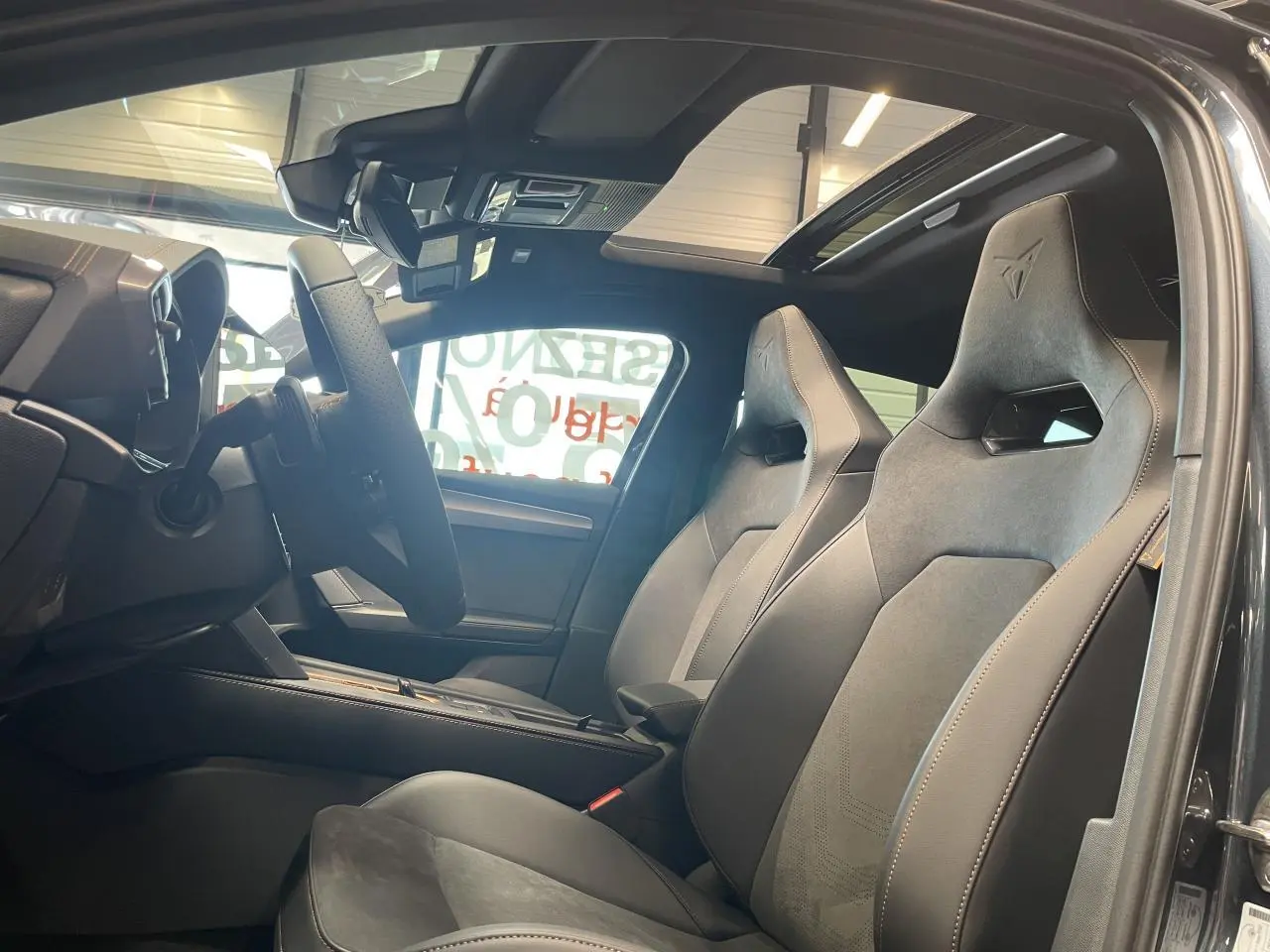 Vue intérieure côté conducteur de la CUPRA Leon 2026 gris magnetic, sièges baquets suédine noire avec surpiqûres cuivrées.