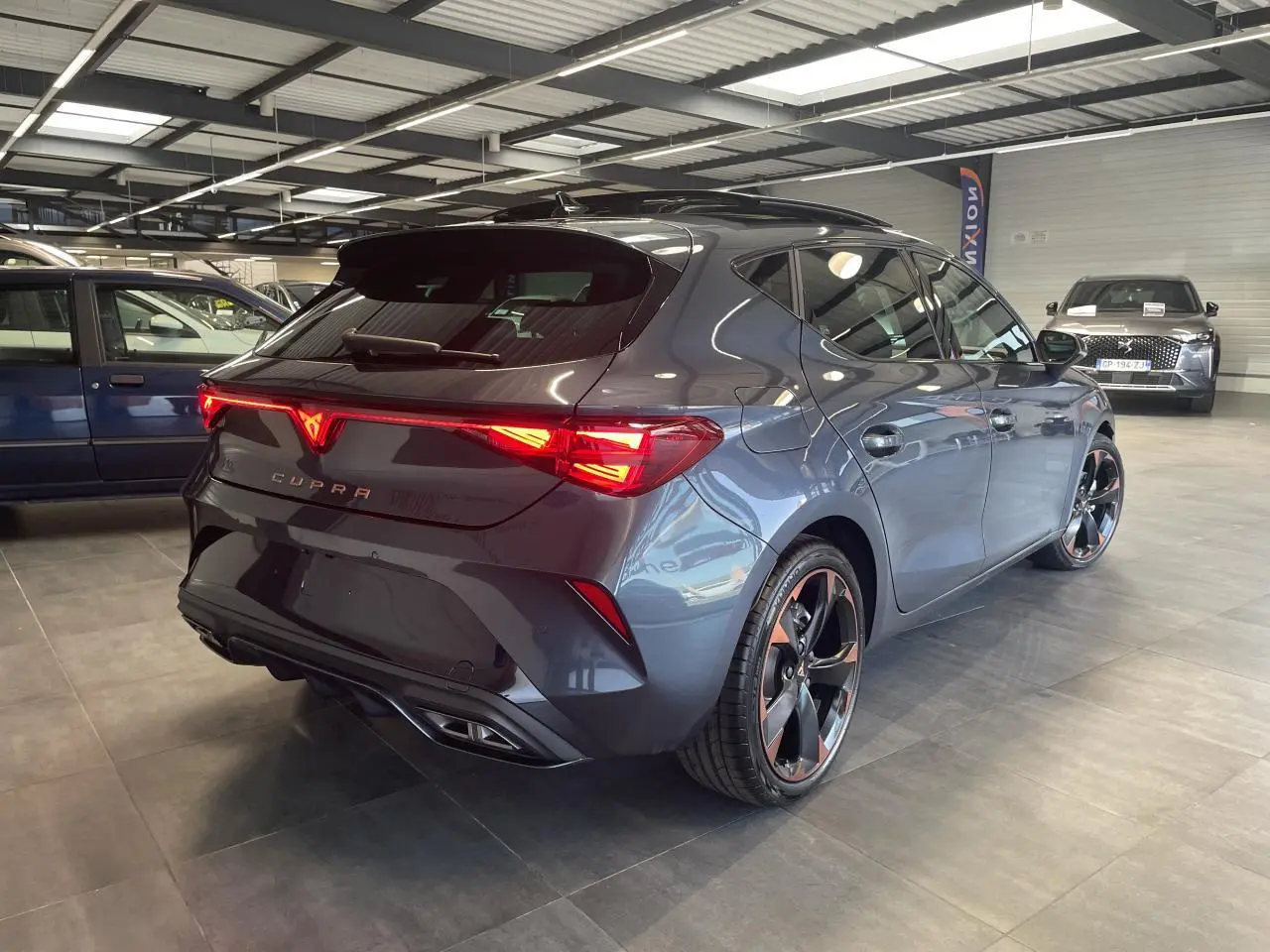 Vue 3/4 arrière droite d'une CUPRA Leon gris magnetic avec feux arrière Tri-LED et jantes cuivrées 18 pouces.