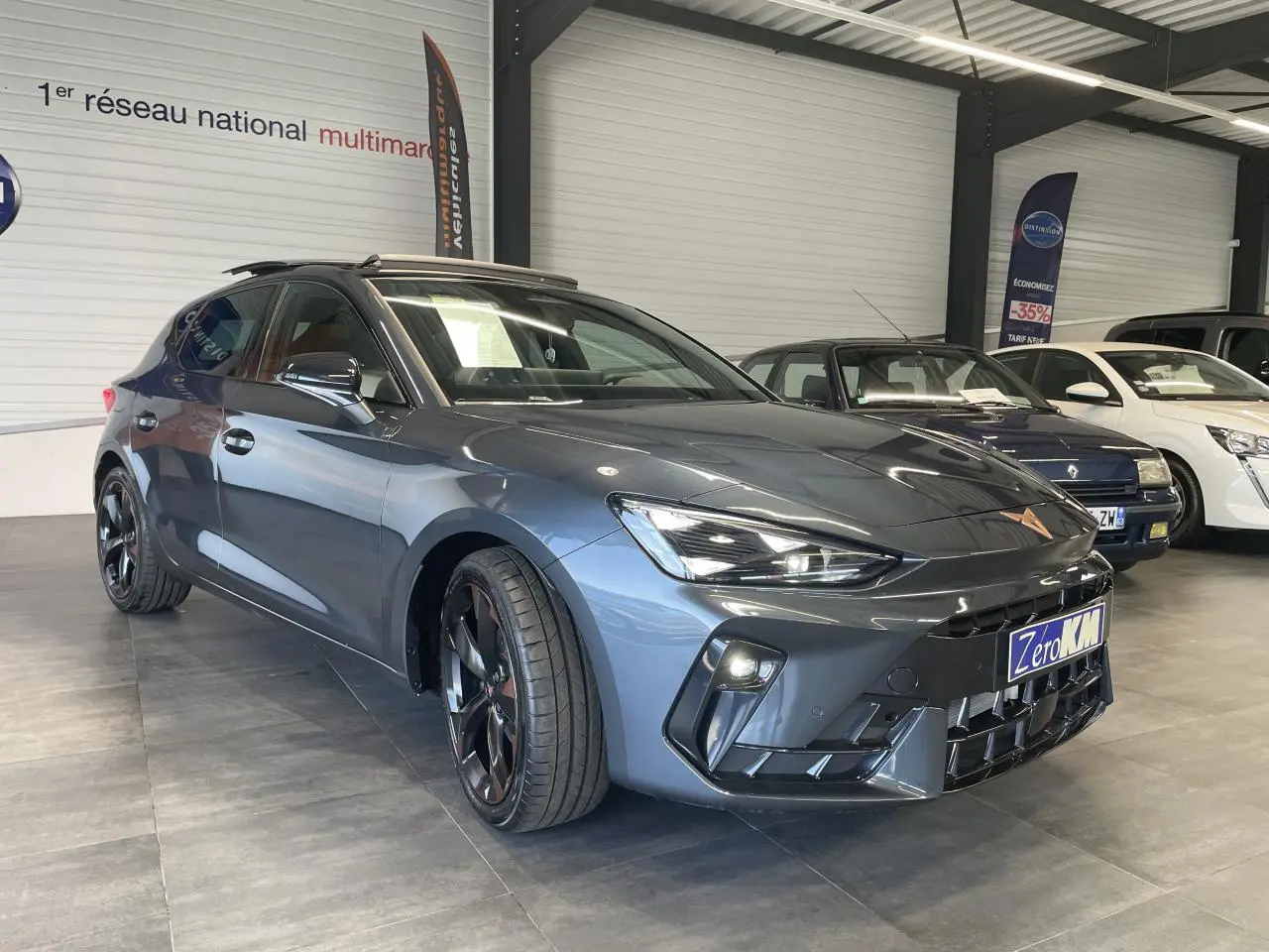 Vue 3/4 avant d'une CUPRA Leon 2.0 TDI gris magnetic avec jantes cuivrées dans un showroom intérieur.