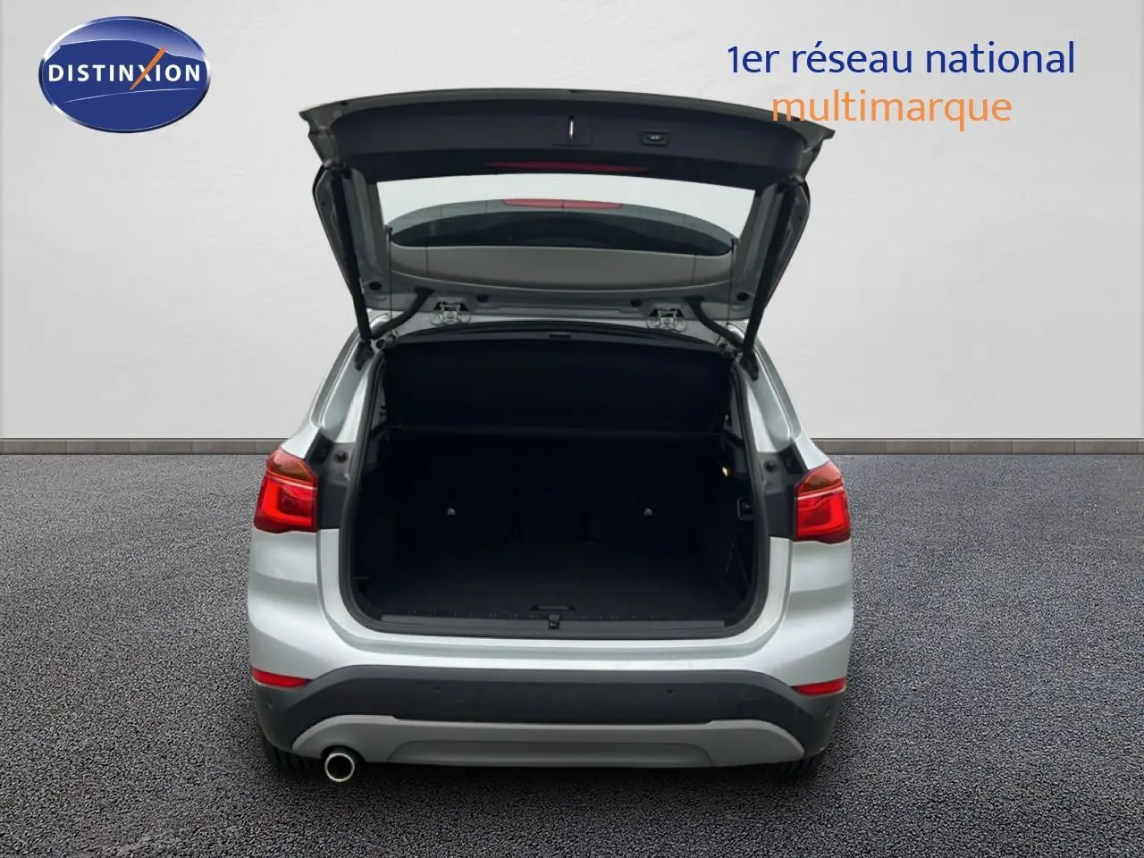 Vue arrière d’un BMW X1 gris argent métal 2018 avec le coffre ouvert, montrant l’espace de chargement vide.