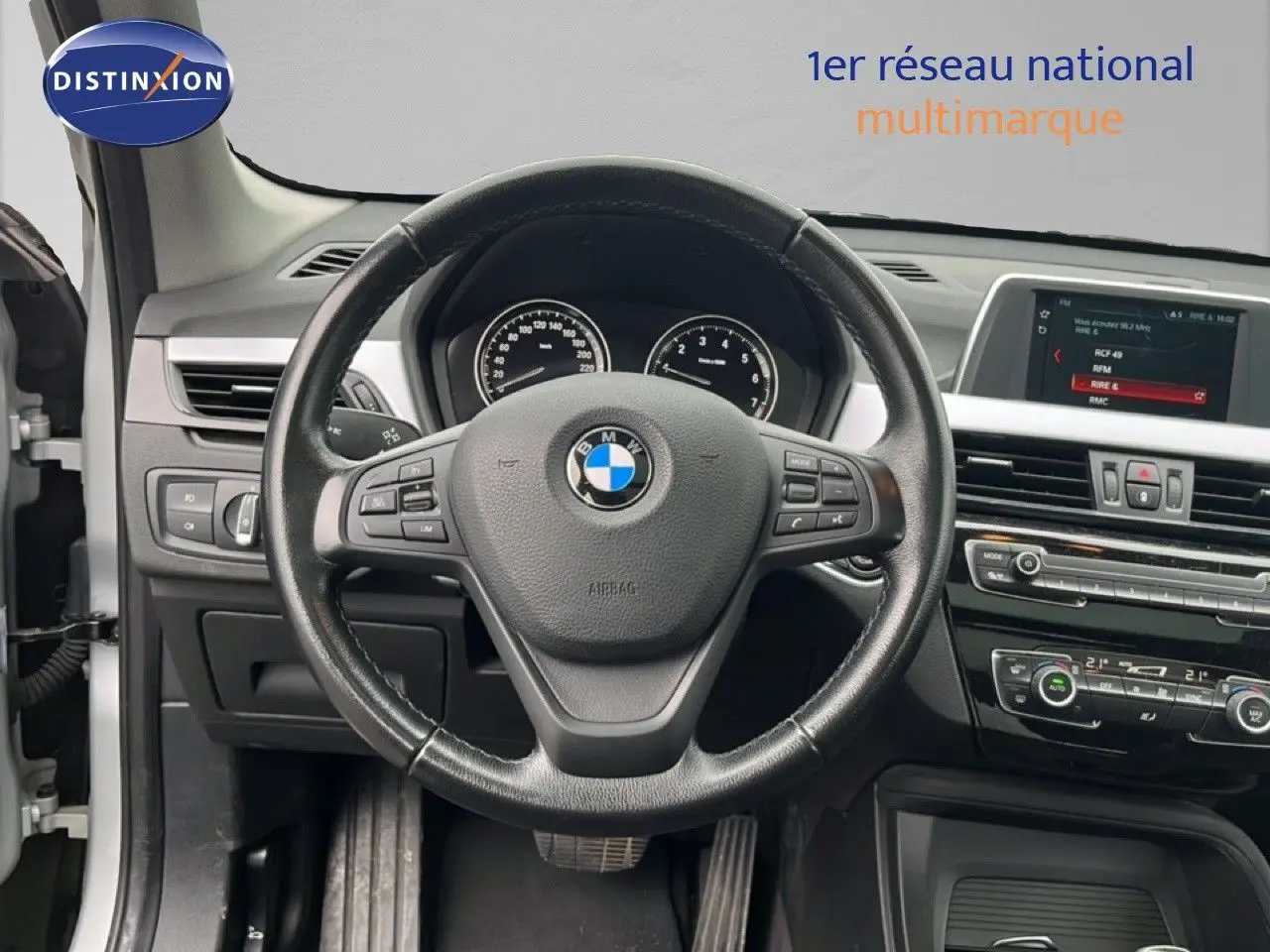 Vue intérieure centrée sur le volant noir de la BMW X1 18i 2018 avec tableau de bord et écran multimédia visibles.