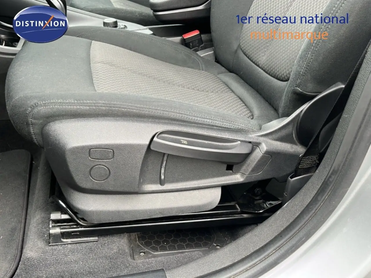 Gros plan sur le siège avant droit en tissu gris noir d’un BMW X1 gris argent métal, avec réglages manuels visibles.