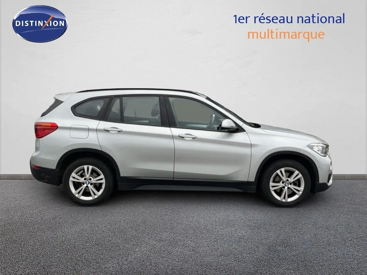 BMW X1 18i gris argent métal vu de profil côté gauche, avec jantes alliage 17 pouces et cinq portes visibles.