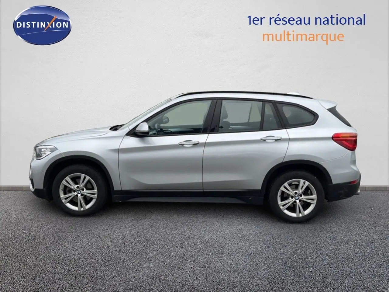 Profil côté gauche d'un BMW X1 18i gris argent métallisé, avec jantes alliage et lignes épurées visibles.