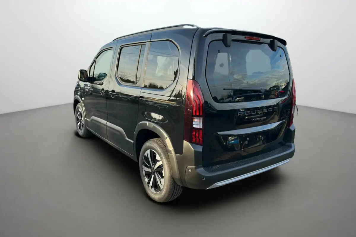 Vue 3/4 arrière droite du Peugeot Rifter noir perla nera avec barres de toit et jantes alu 17 pouces visibles.