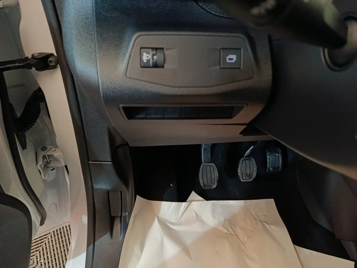 Vue intérieure côté conducteur du Peugeot Partner blanc 2026, montrant les pédales et les commandes sous le tableau de bord.