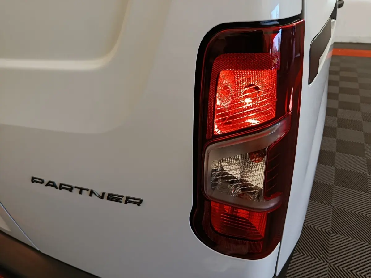 Gros plan sur le feu arrière droit d’un Peugeot Partner blanc, avec le logo PARTNER visible sur la porte arrière.