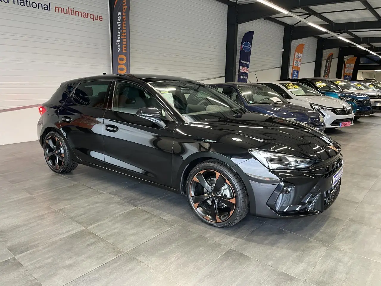 Vue 3/4 avant d'une CUPRA Leon noire avec jantes alliage 18'' cuivrées dans un showroom intérieur.