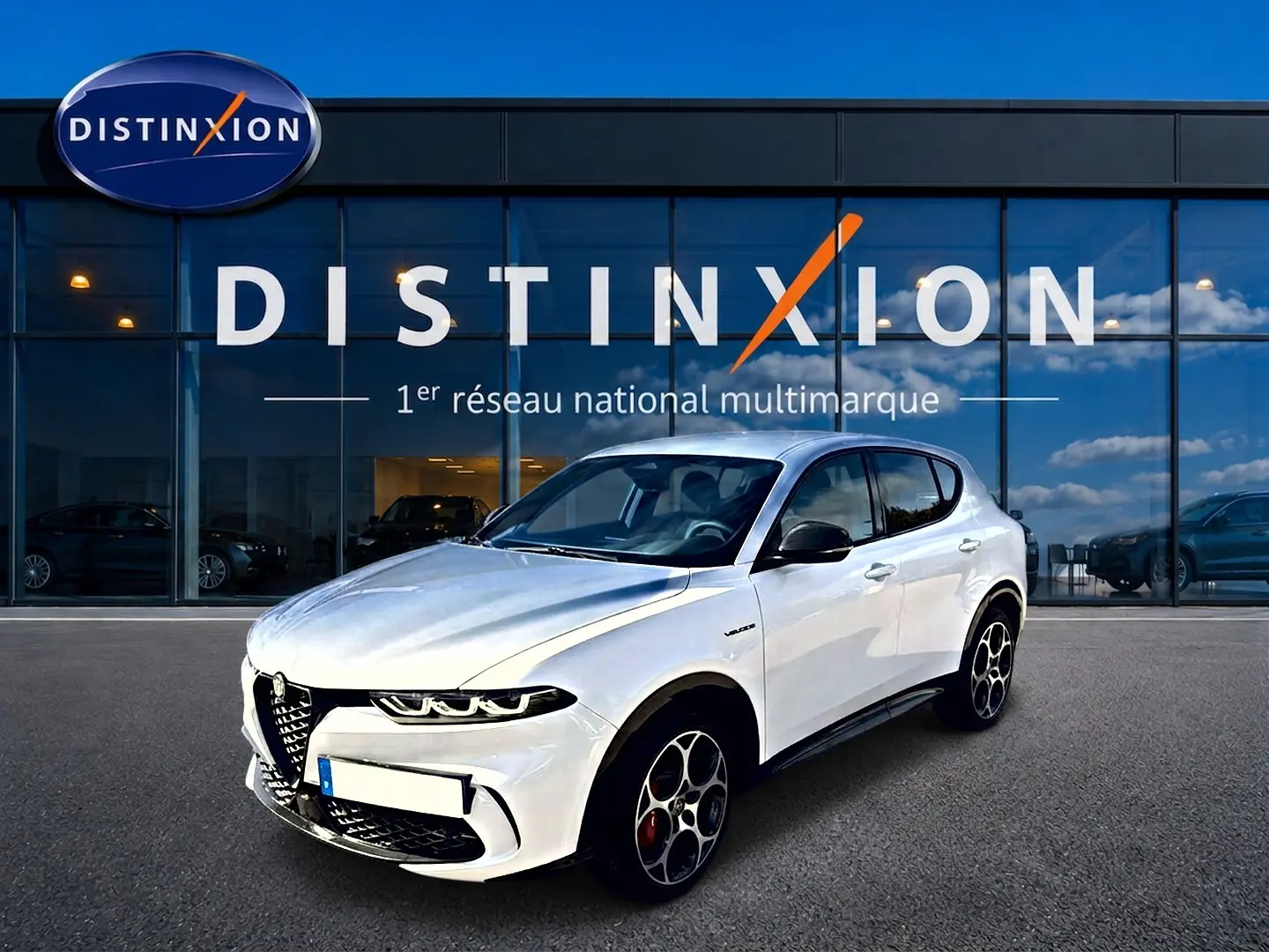 Vue 3/4 avant d'une Alfa Romeo Tonale blanche avec jantes alu distinctives, stationnée devant une vitrine Distinxion.