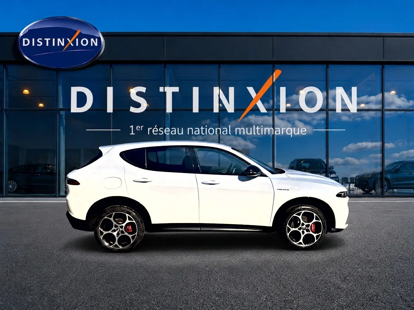 Vue de profil côté gauche d'un Alfa Romeo Tonale blanc avec jantes alu et étriers rouges, devant une vitrine Distinxion.