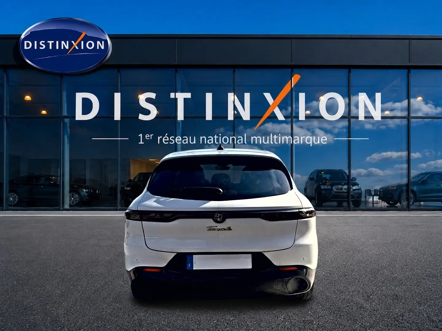 Vue arrière d'une Alfa Romeo Tonale blanche 2025 garée devant une vitrine avec logo Distinxion.