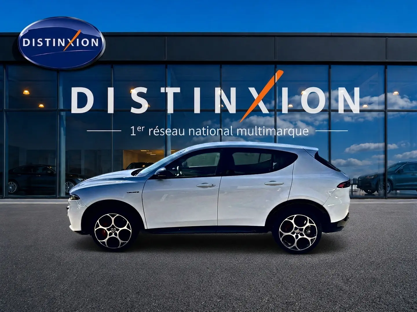 Vue de profil côté gauche d'un Alfa Romeo Tonale blanc 2025 garé devant une vitrine Distinxion.
