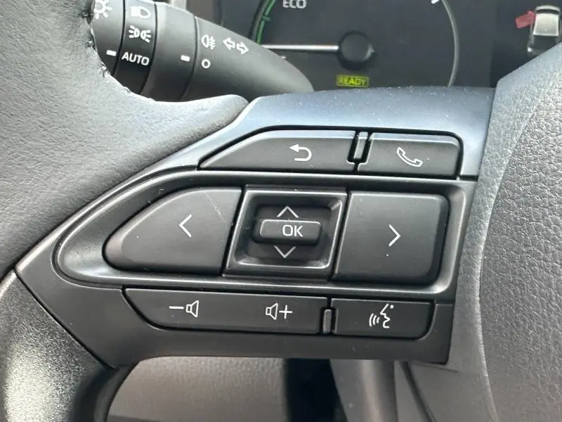 Gros plan sur les commandes multifonctions noires au volant d'une Toyota Yaris blanche 2025 hybride essence.