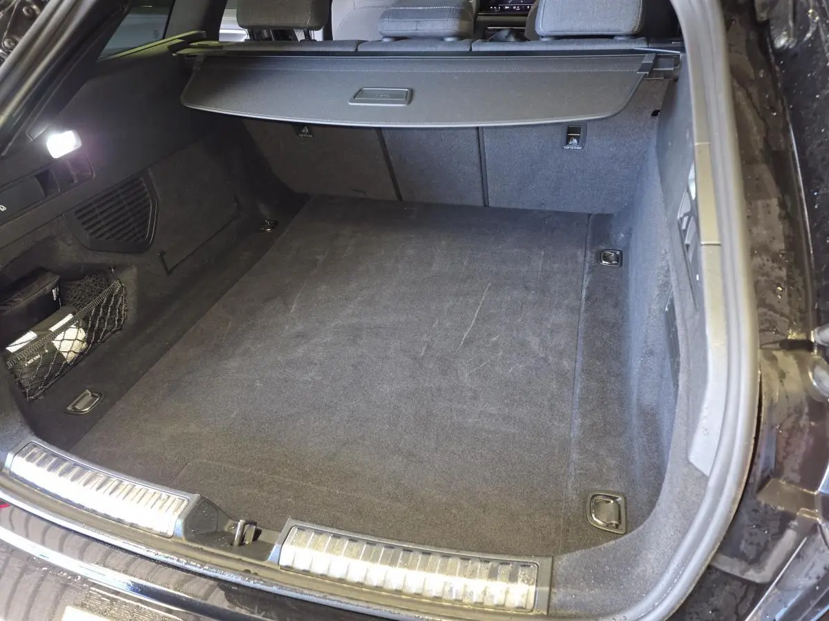 Coffre ouvert vu de l’arrière d’une Audi A5 Avant noir, avec tapis de sol et filet de rangement latéral.